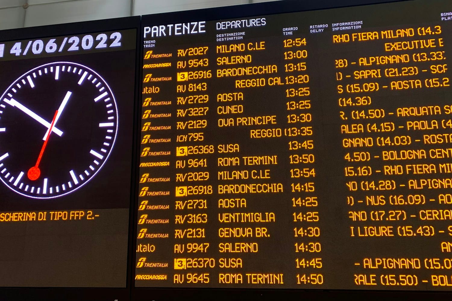 A train station departure board with a large clock