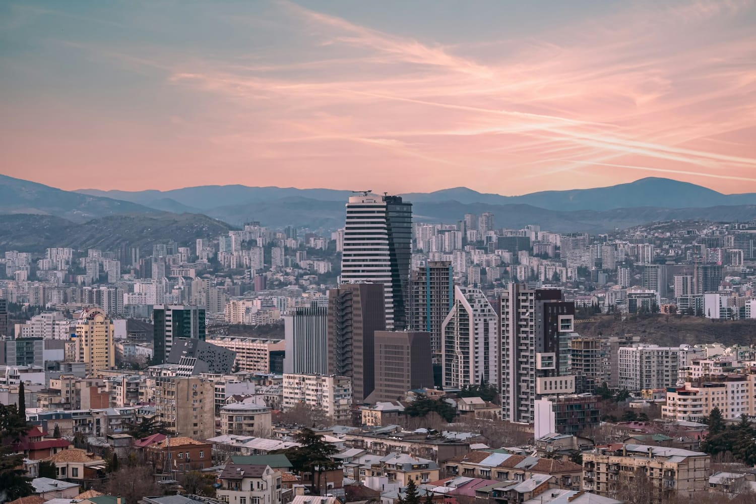 Modern office towers rising above Tbilisi at dusk, with mountains behind