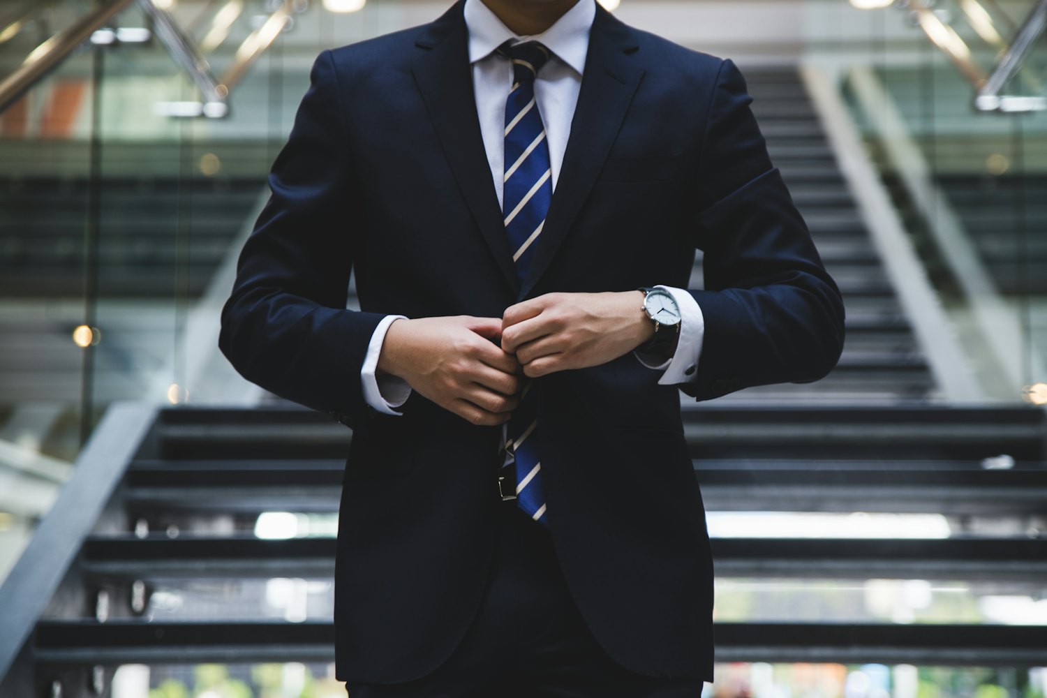 A man in a dark suit buttoning his jacket in a modern building