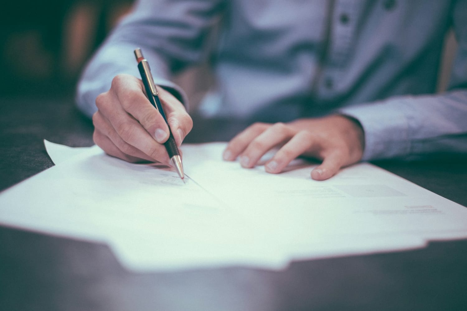 A man signing a document with a pen at a desk