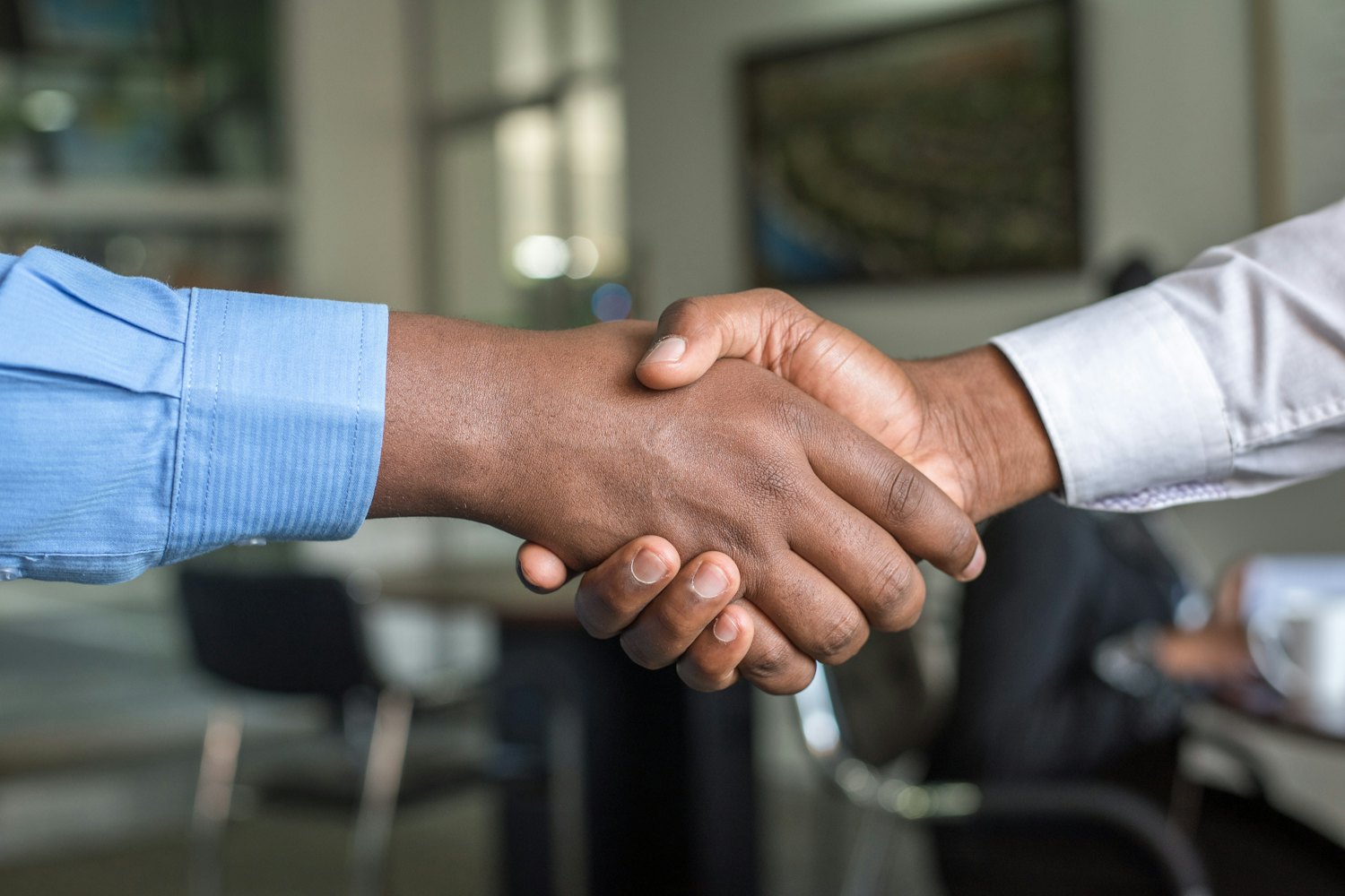 Two business people shaking hands across a meeting room