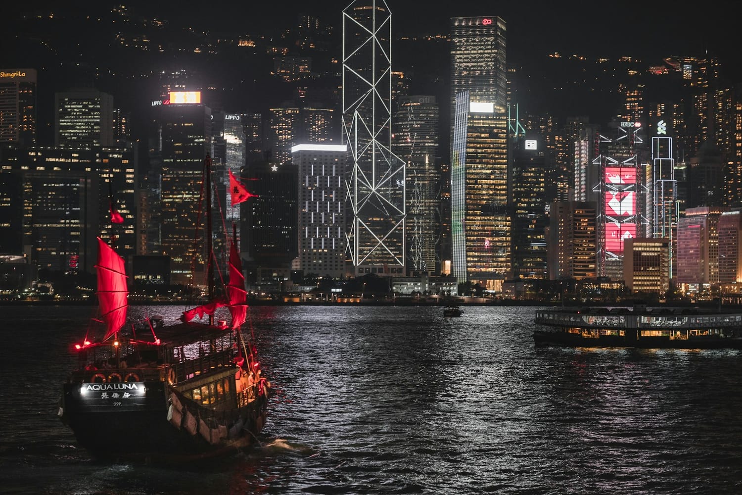 A traditional junk with red sails crossing Victoria Harbour at night