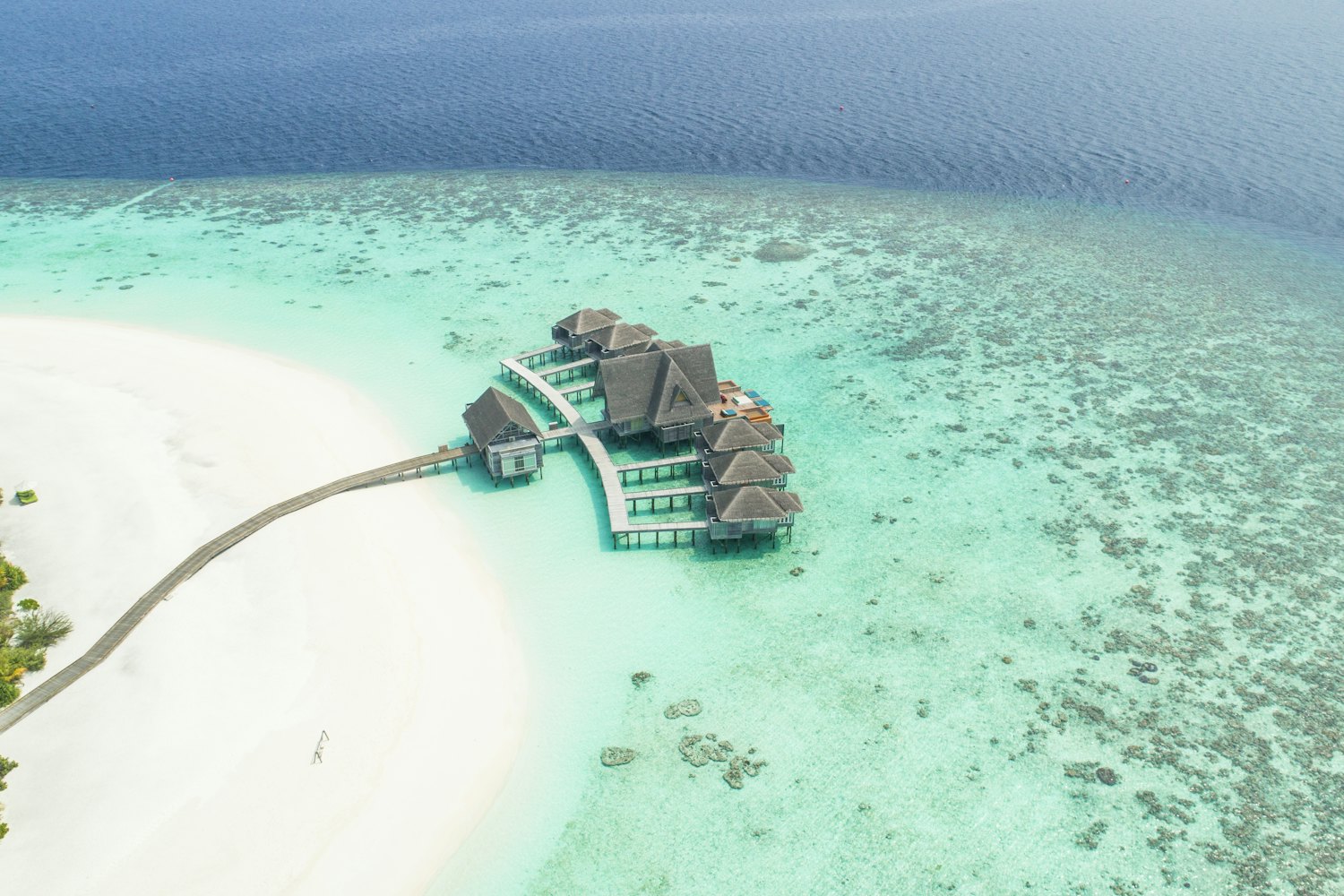 Aerial view of turquoise shallows, a white sand spit and overwater bungalows