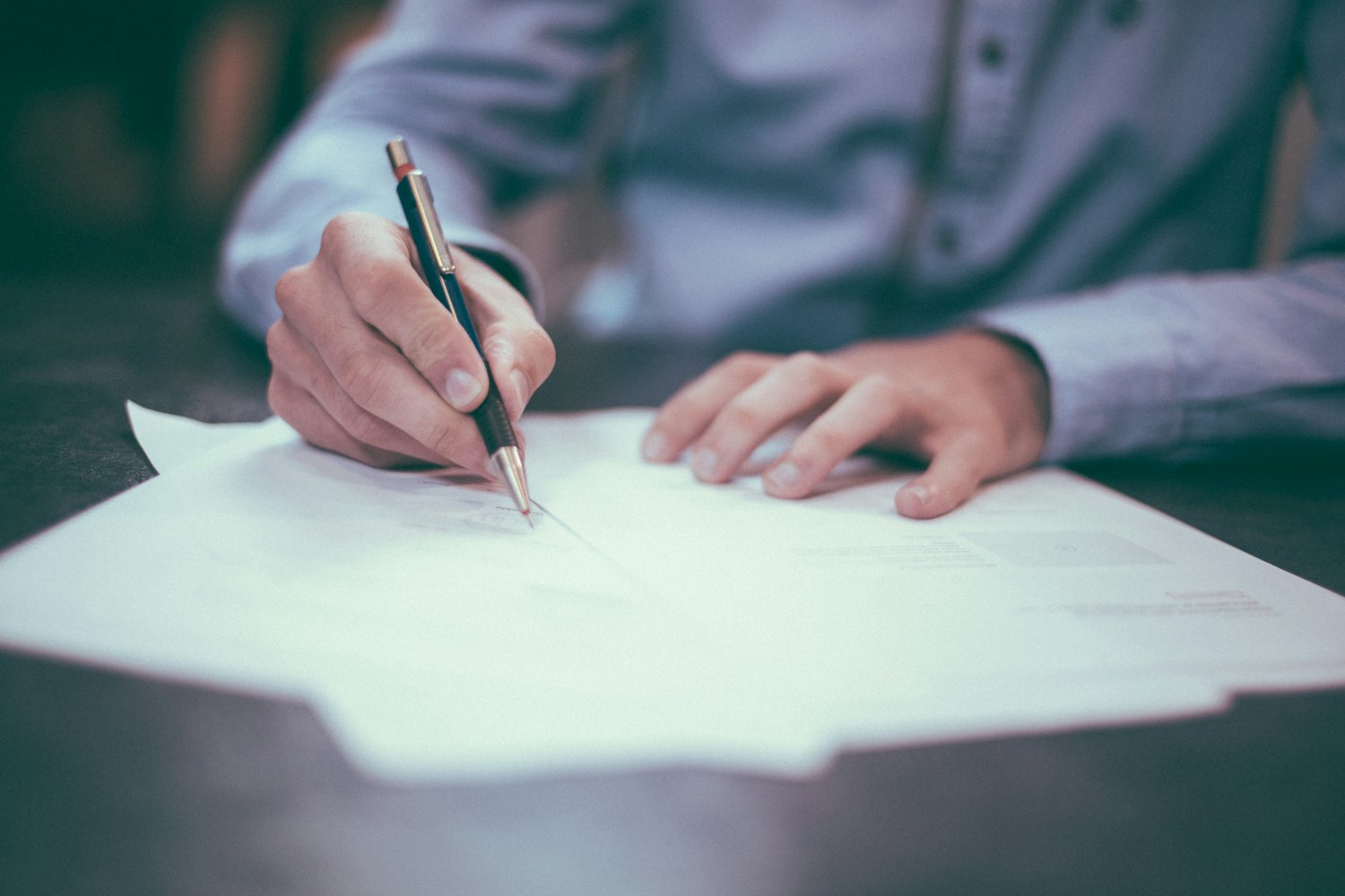 Person unterschreibt ein Dokument mit einem Stift am Schreibtisch