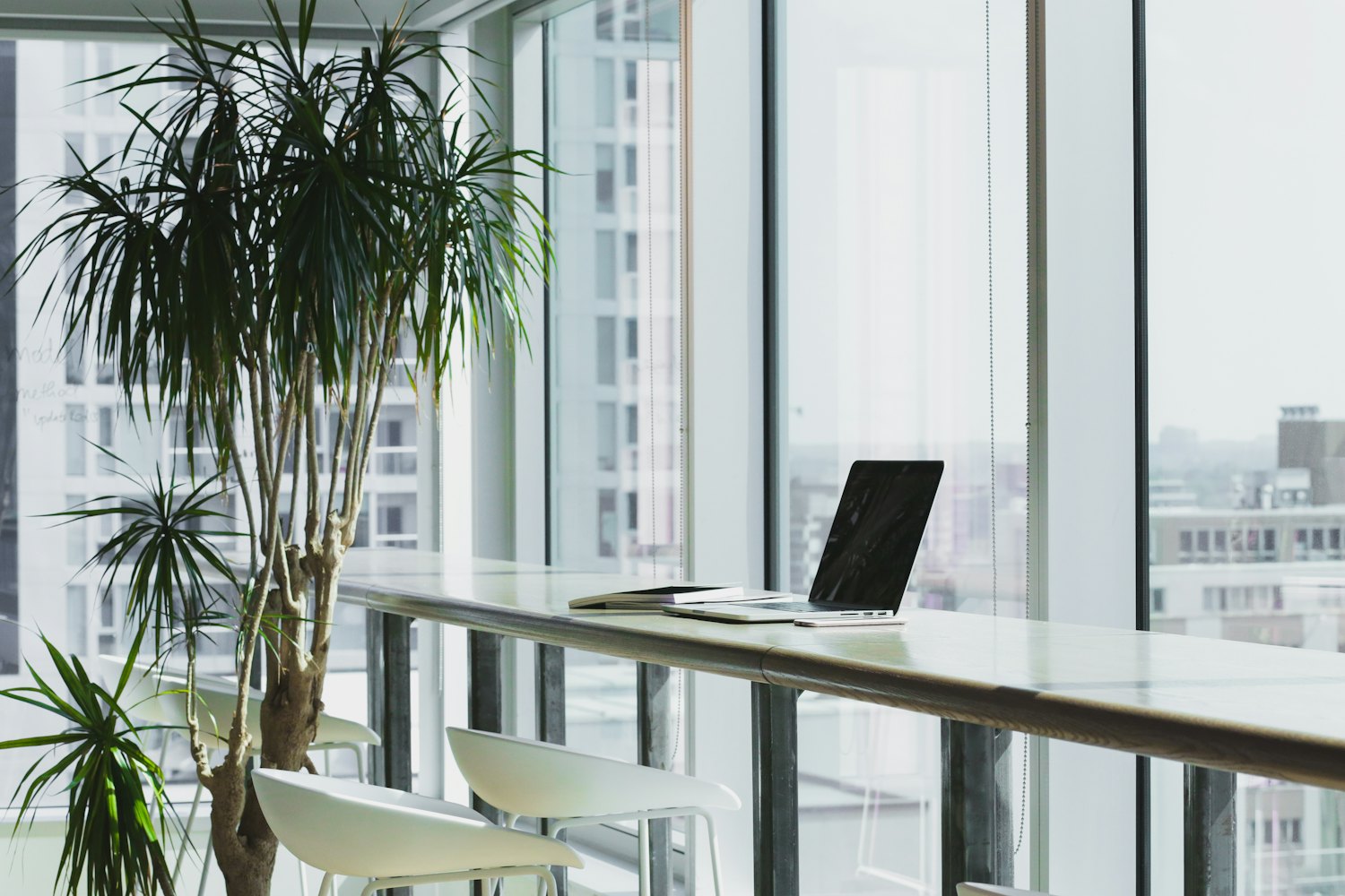 Helles Büro mit einem Laptop auf einem langen Tisch an raumhohen Fenstern