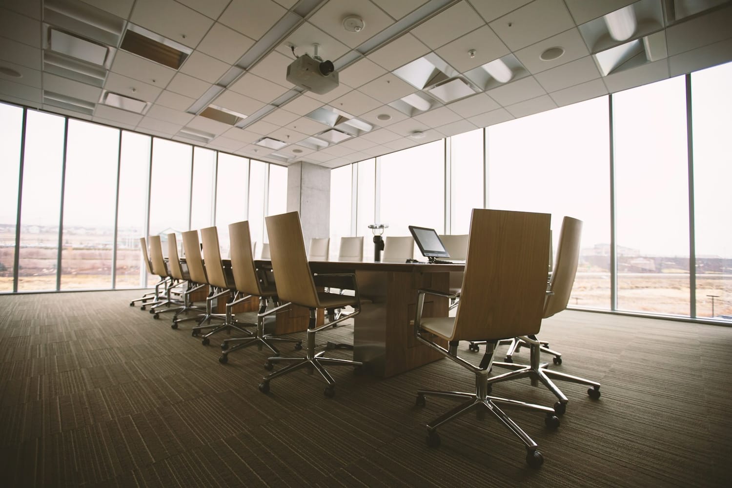 An empty boardroom with a long table and leather chairs facing large windows